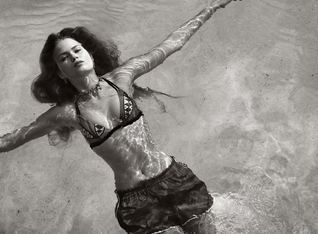 Monochrome shot of a woman in bikini and shorts floating in water, arms outstretched, creating a serene and peaceful atmosphere.