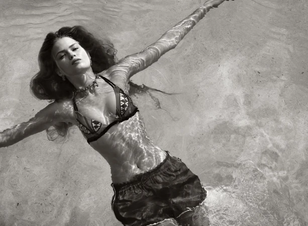 Monochrome shot of a woman in bikini and shorts floating in water, arms outstretched, creating a serene and peaceful atmosphere.