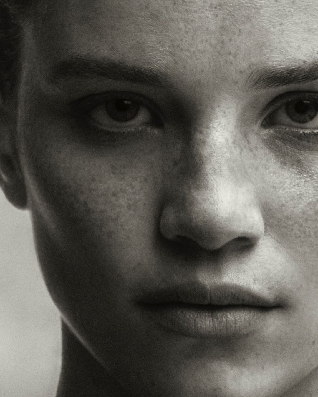Close-up monochrome portrait of a woman with prominent freckles photographed by Christian Macdonald