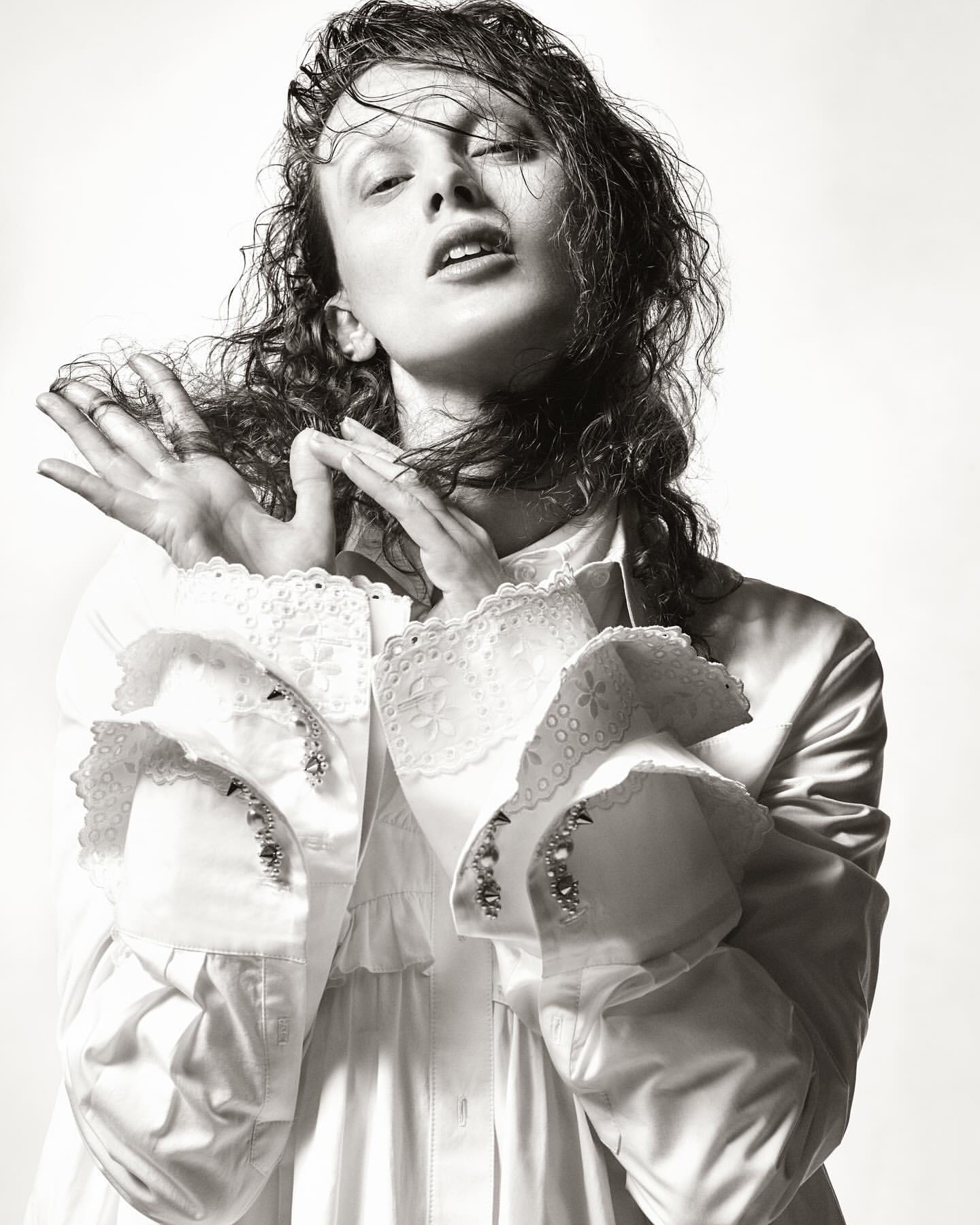 Model with wet hair wearing a white shirt with ruffled cuffs posing against a plain background