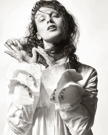 Model with wet hair wearing a white shirt with ruffled cuffs posing against a plain background