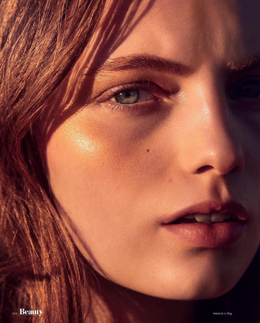 Close-up of a young woman with copper-red hair and green eyes, featuring soft, golden-toned lighting and focus on beauty and skincare.