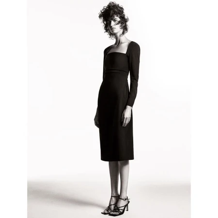 Fashion model wearing a black, long-sleeved midi dress and strappy heels in a studio shot on a white backdrop, fashion editorial.
