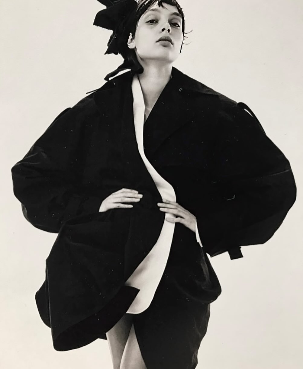 Fashion shot of a woman in black jacket with white accents posing in front of a white background in a studio. Editorial look.