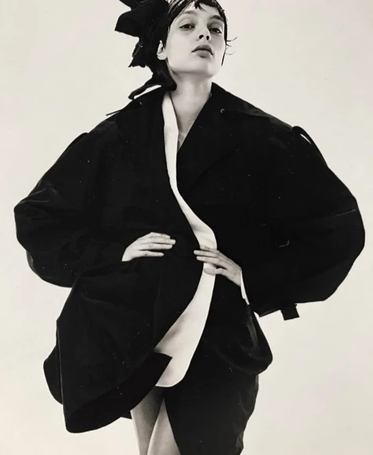 Fashion shot of a woman in black jacket with white accents posing in front of a white background in a studio. Editorial look.