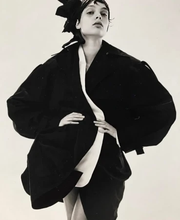 Fashion shot of a woman in black jacket with white accents posing in front of a white background in a studio. Editorial look.