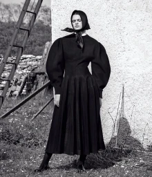 Model in black puff sleeve dress and silk headscarf standing outdoors near a stone wall by Christian Macdonald