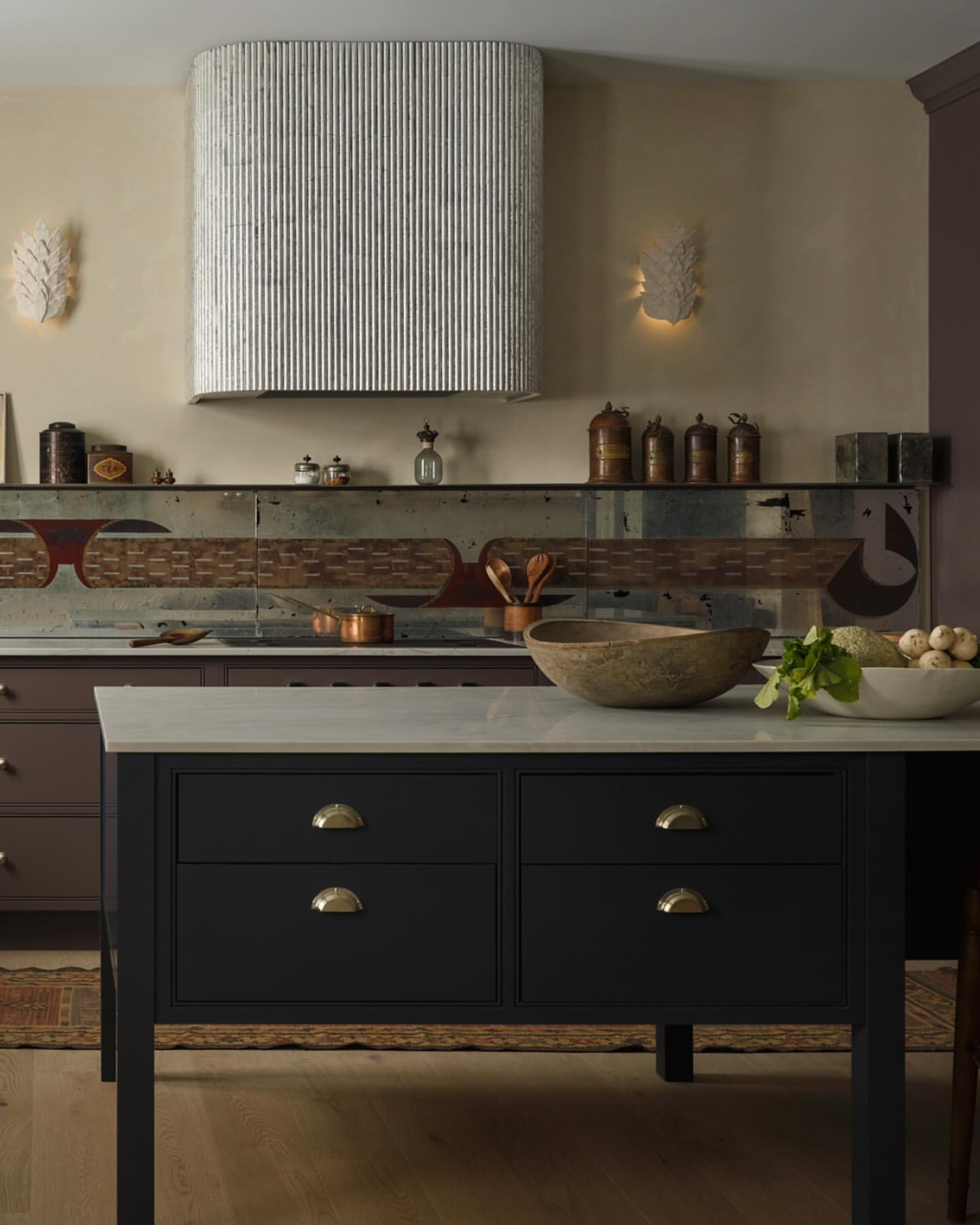 Kitchen interior featuring a black kitchen island with a marble countertop, wooden bowls, and white walls with sconces.