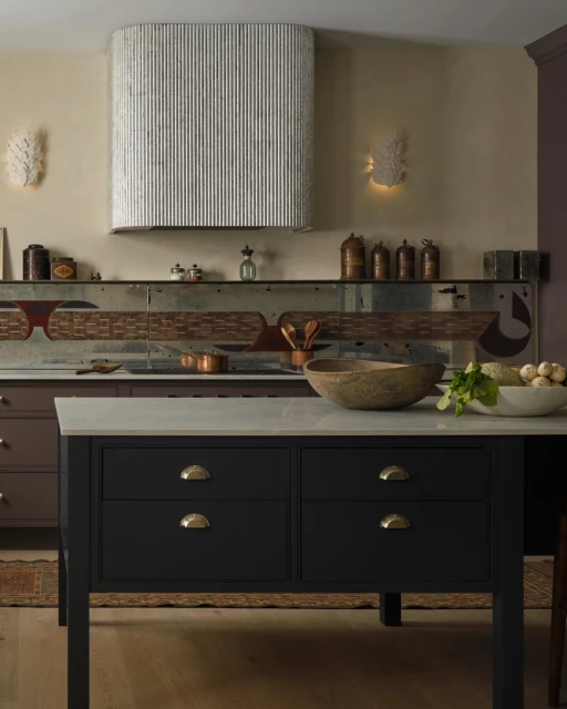 Kitchen interior featuring a black kitchen island with a marble countertop, wooden bowls, and white walls with sconces.