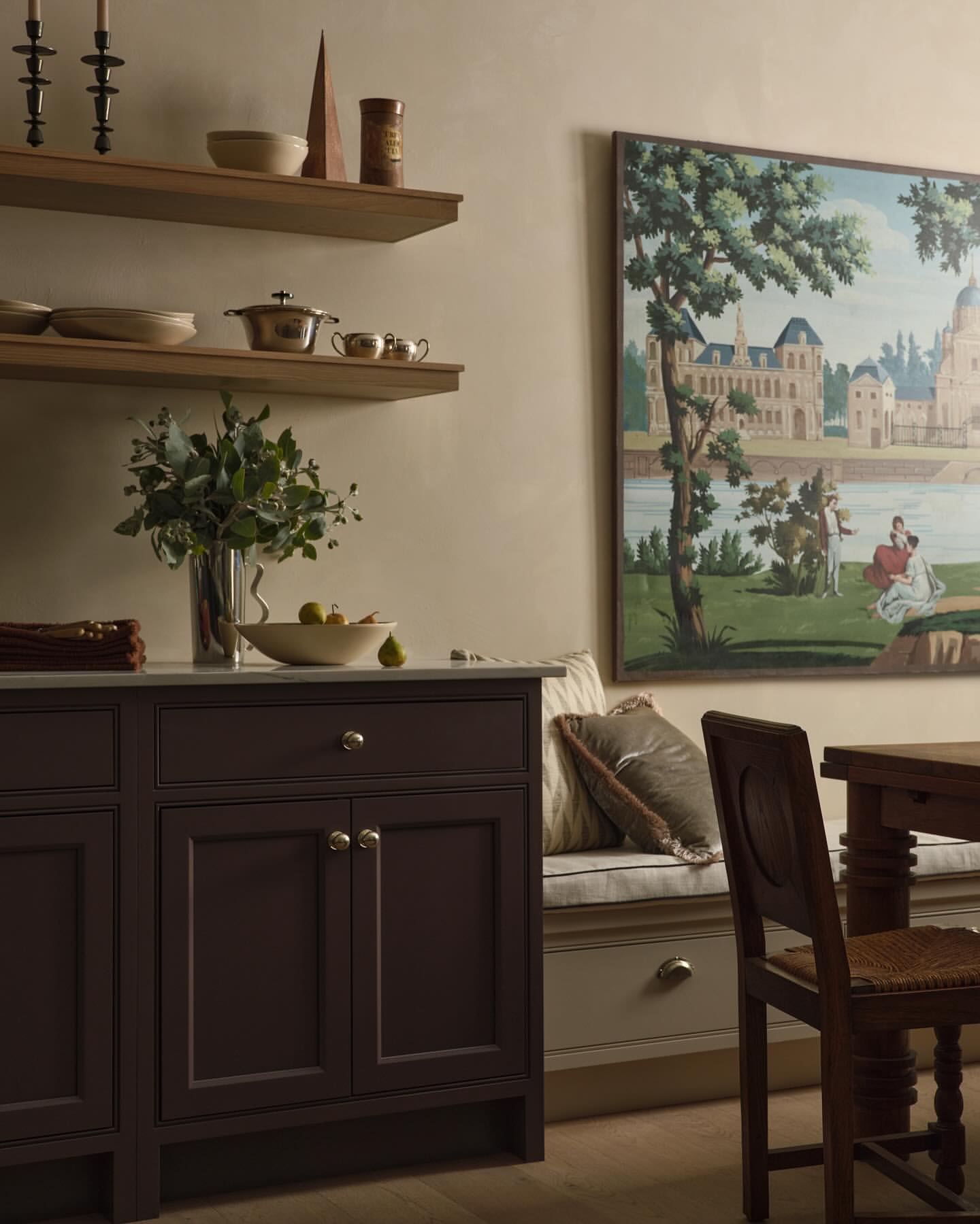 Traditional dining area featuring a dark-stained cabinet, a framed landscape painting, shelves with decor, and a wooden table and chair.