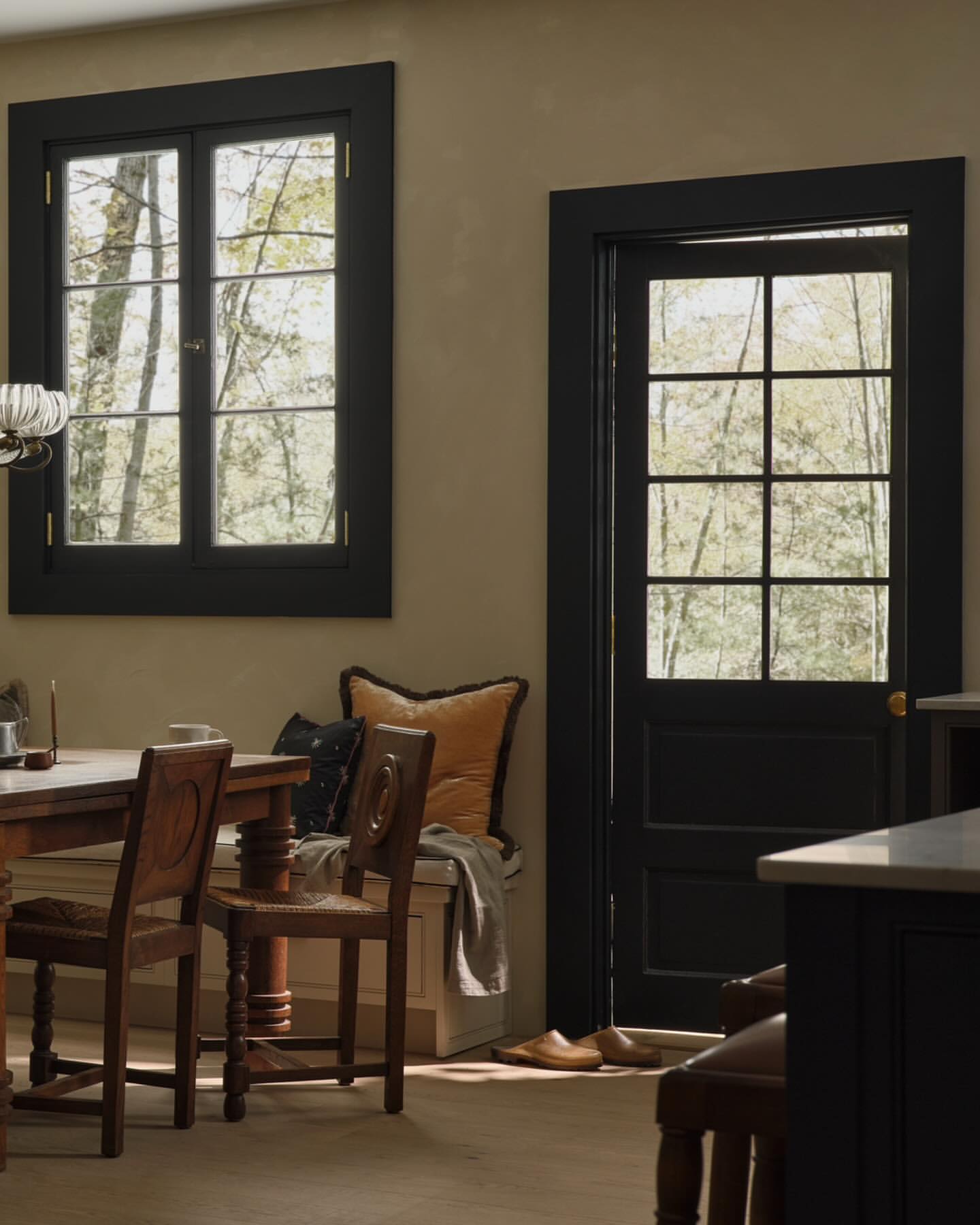 Interior view showcases a wooden table and chairs near a window and door with natural light filtering through, creating a cozy ambiance.