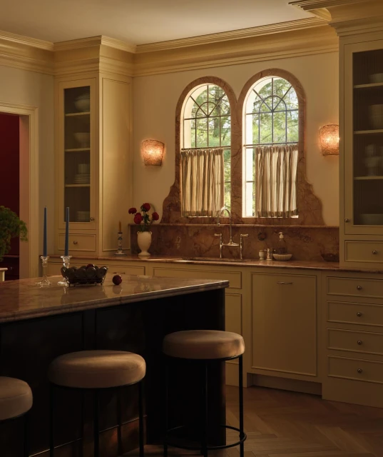 Elegant kitchen interior with brown granite countertops, a dark island with stools, and arched windows with natural light.