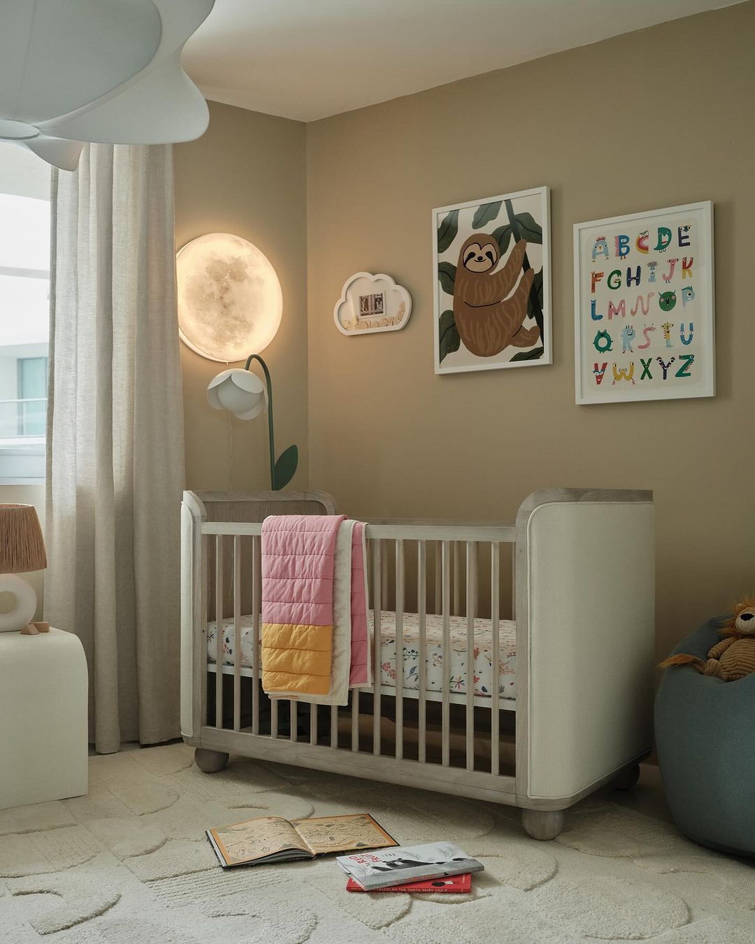 Neutral-toned nursery featuring a white baby crib, a moon-shaped lamp, framed animal art, and a soft white rug. Interior photography.