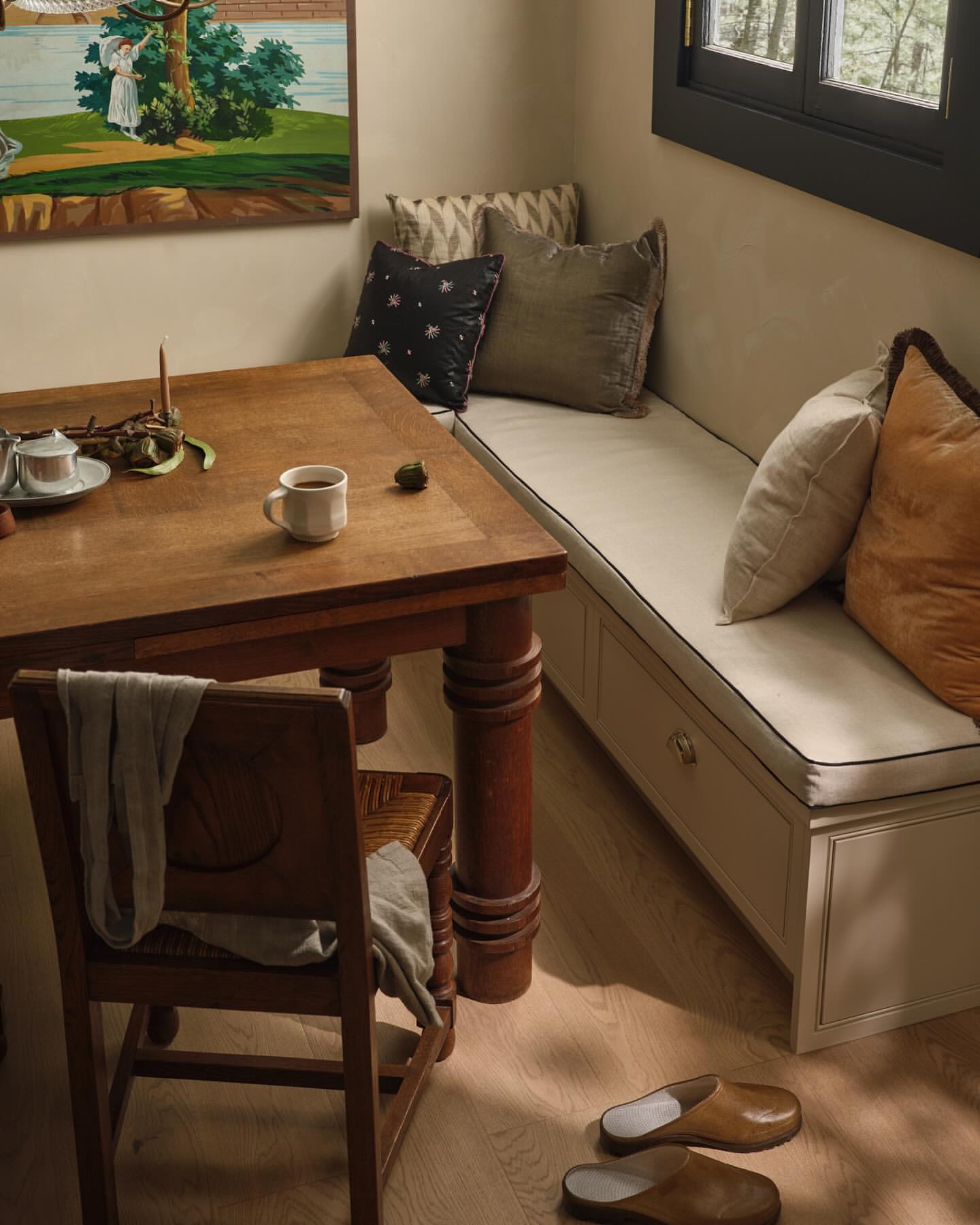 Interior of a home with a wooden table and chair next to a cushioned bench, complemented by decorative pillows and natural lighting.