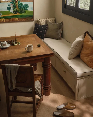 Interior of a home with a wooden table and chair next to a cushioned bench, complemented by decorative pillows and natural lighting.