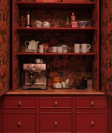 Interior view of a red cabinet with open doors revealing shelves filled with teacups, bowls, an espresso machine, and decorative objects.