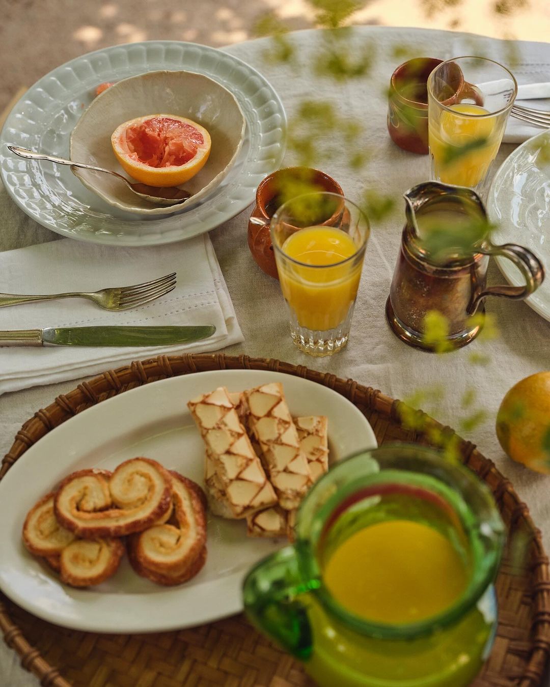 Overhead shot of a breakfast table featuring pastries, sliced grapefruit, and orange juice in pitchers and glasses, all bathed in natural light.
