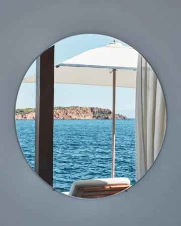 Seascape view through a round opening with a beach umbrella, ocean water, and rocky land mass in the background on a sunny day.