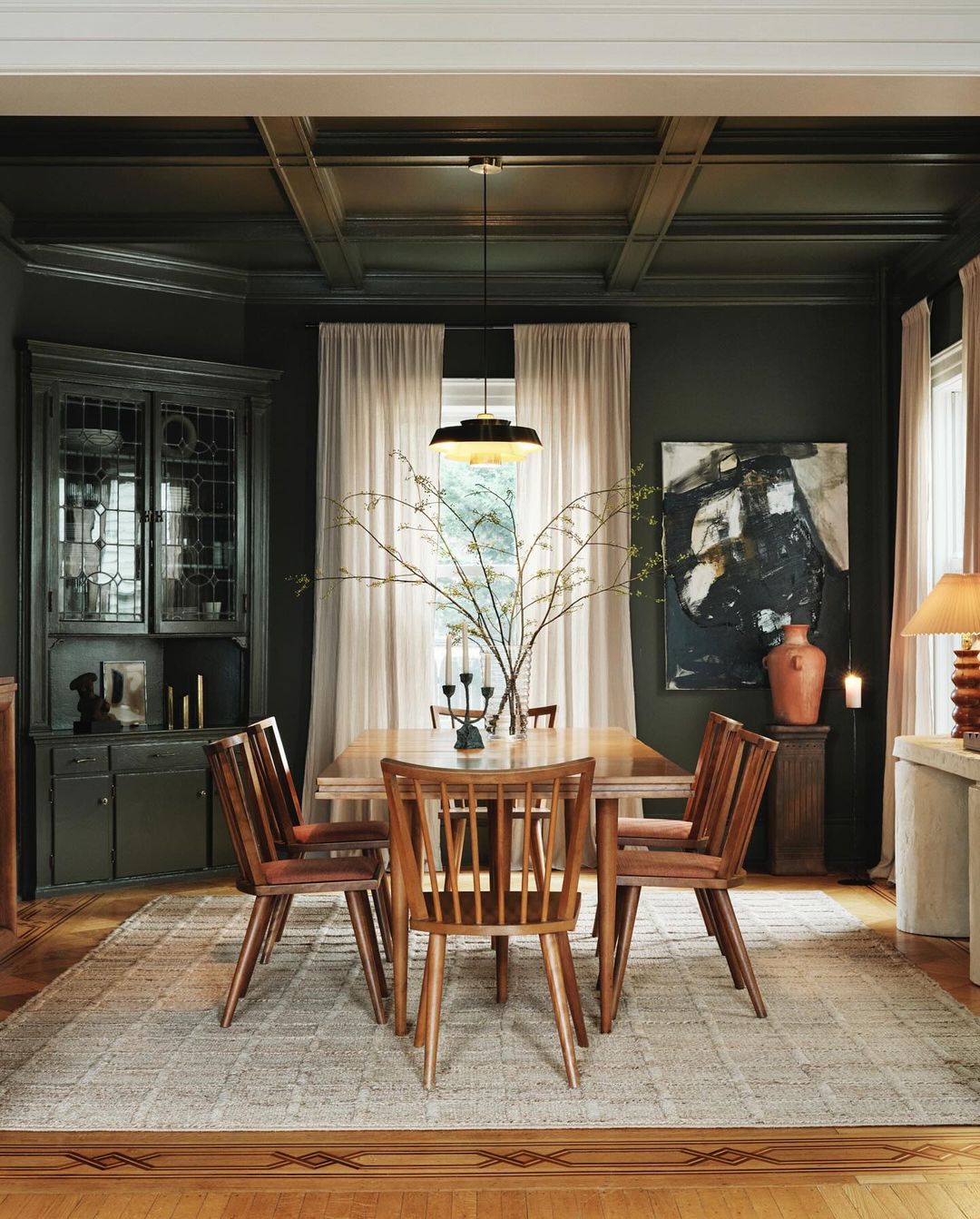 Interior view of a dining room featuring a wooden table and chairs, with natural light filtering through sheer curtains.