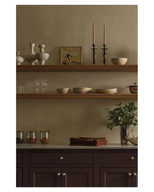Rustic interior featuring shelves with ceramic vases, wooden bowls, candlesticks, and a framed print above brown kitchen cabinets.