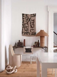 Interior shot featuring a wooden carved chair, a console table with objects, a woven lamp, and a wall hanging by Christian Torres