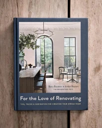 Closed navy blue hardcover book titled For the Love of Renovating resting flat on a rustic wooden plank surface.