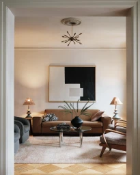 Interior shot of a living room featuring a brown sofa, glass coffee table, and large abstract painting.