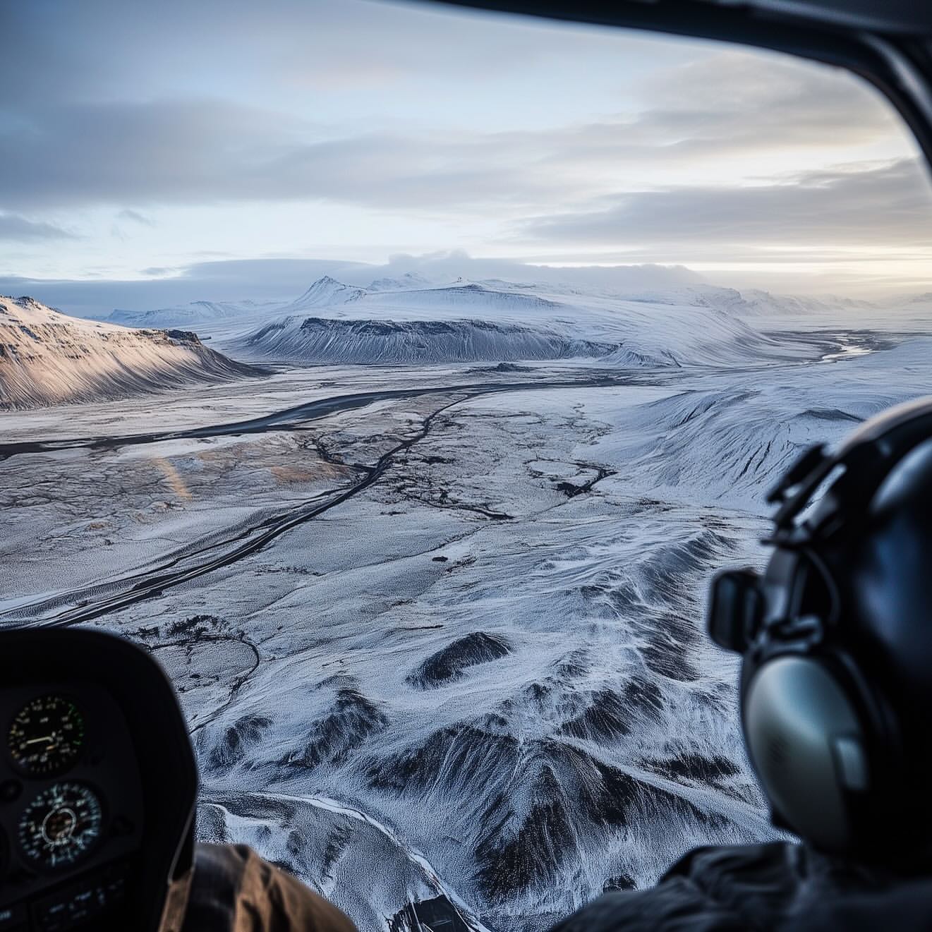 Aerial view from helicopter cockpit: A vast snow-covered landscape, mountains, and cloudy sky fill the scene, cockpit interior.