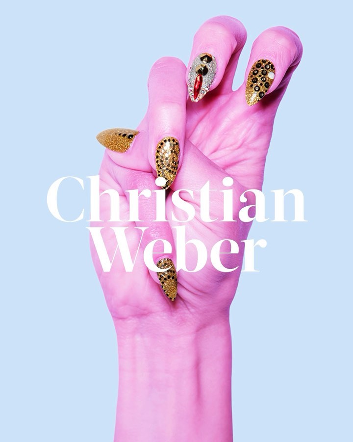 Woman's hand with designer gold and silver embellished nails posing in a studio with soft pink skin tones against a light blue background.