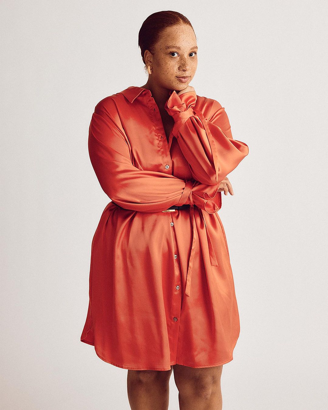 Portrait of a woman in a coral dress with a belt, posing in a studio against a neutral background, showcasing fashion and style.