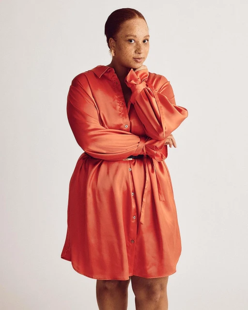Portrait of a woman in a coral dress with a belt, posing in a studio against a neutral background, showcasing fashion and style.