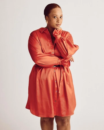 Portrait of a woman in a coral dress with a belt, posing in a studio against a neutral background, showcasing fashion and style.