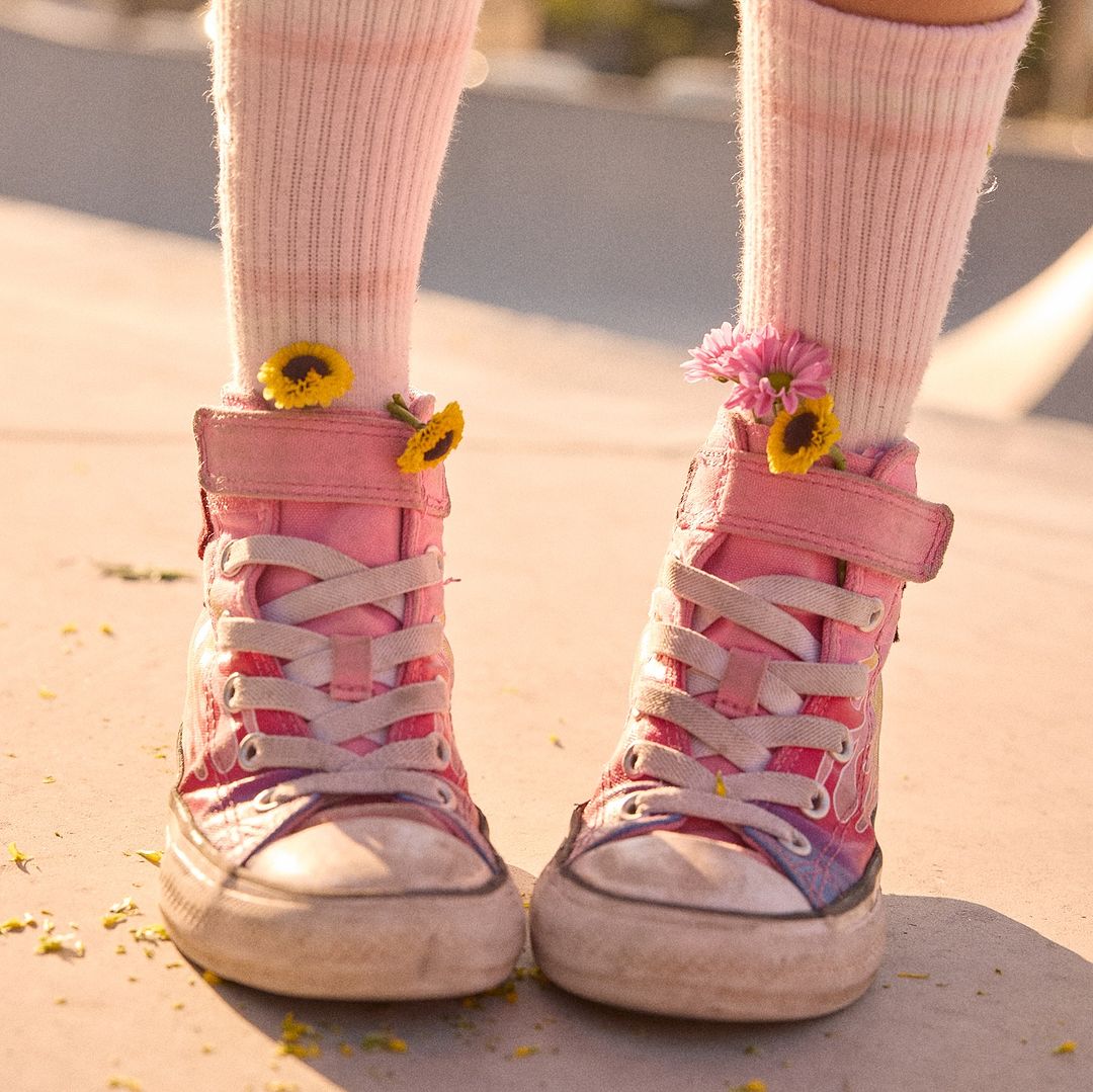 Close-up of pink high-top sneakers decorated with fresh flowers, paired with white socks, showcasing a creative footwear design.