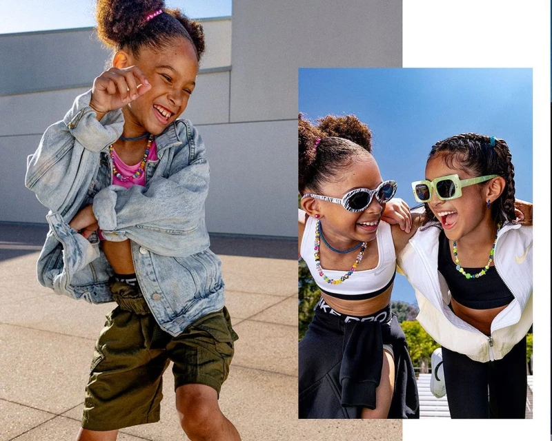 Two happy young girls in casual activewear and sunglasses laugh together outdoors on a sunny day, dressed in the latest fashion trends.