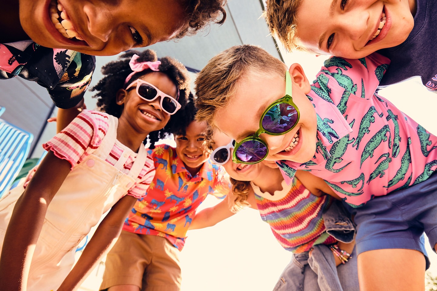 Group of smiling children in sunglasses looking down at the camera, wearing colourful casual clothes, summer fashion, happy kids.