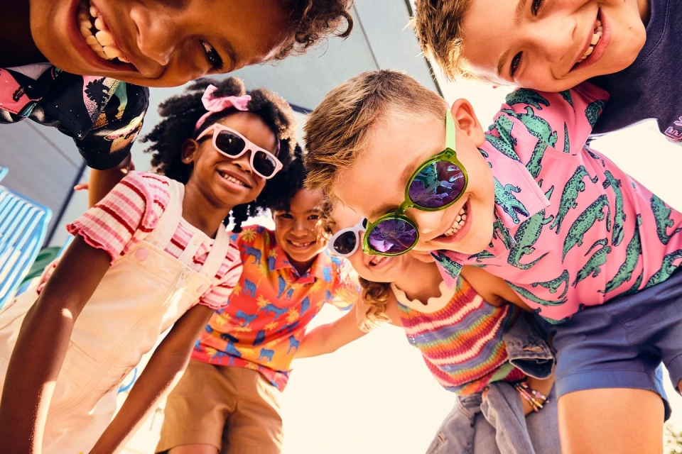 Group of smiling children in sunglasses looking down at the camera, wearing colourful casual clothes, summer fashion, happy kids.