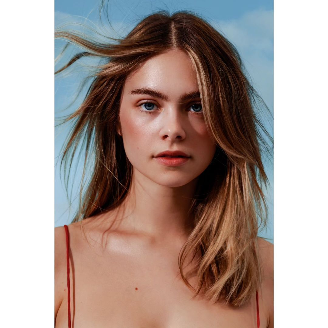 Close-up portrait of a young woman with blonde hair and blue eyes against a soft blue sky background, fashion and beauty concept.