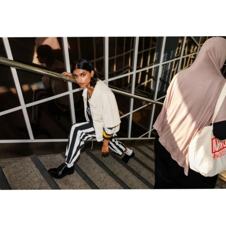 Woman in striped trousers and white jacket descending outdoor stairs alongside someone in a hijab holding a tote bag