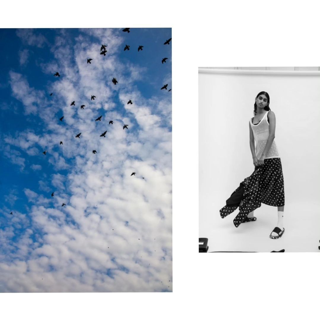 Black and white fashion shot of a model in a white photo studio wearing polka dot pants and a light top next to a blue sky.