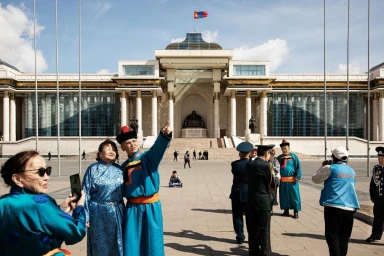 People in traditional Mongolian clothing and modern attire gather in front of a grand classical government building.