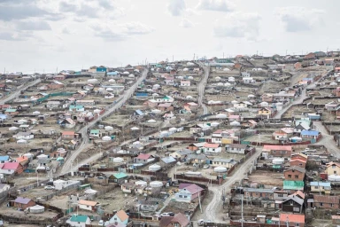 High-angle editorial view of a sprawling hillside settlement with densely clustered houses and round gers under an overcast sky.