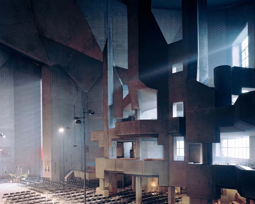 Interior view of the Saint Bernadette du Banlay church in France, featuring brutalist concrete architecture, rows of chairs and natural light.