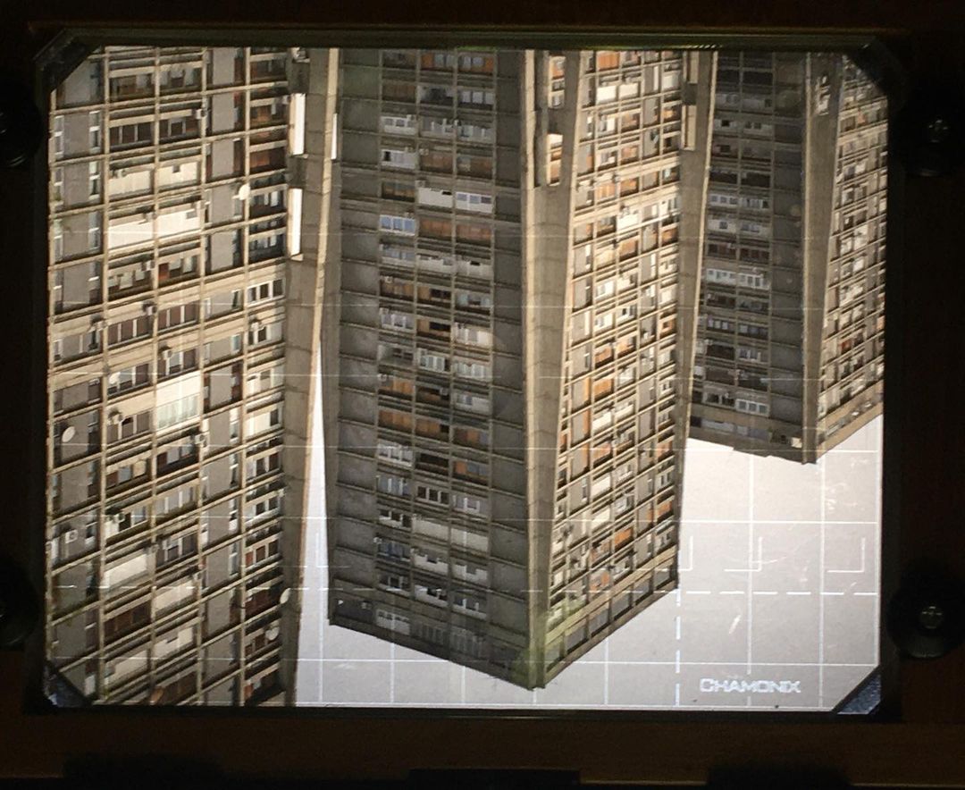 Four tall, brutalist apartment buildings are featured in this architectural study, set against a grid pattern backdrop under artificial lighting.