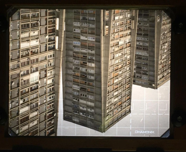 Four tall, brutalist apartment buildings are featured in this architectural study, set against a grid pattern backdrop under artificial lighting.
