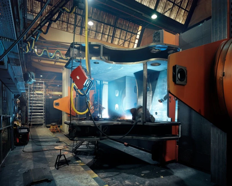 Industrial scene featuring welders working inside a large metal structure in a manufacturing plant, showcasing fabrication and engineering.