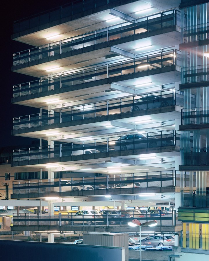 Multi-level parking garage illuminated at night with parked cars on each level. Concrete structure with metal railings and lighting.