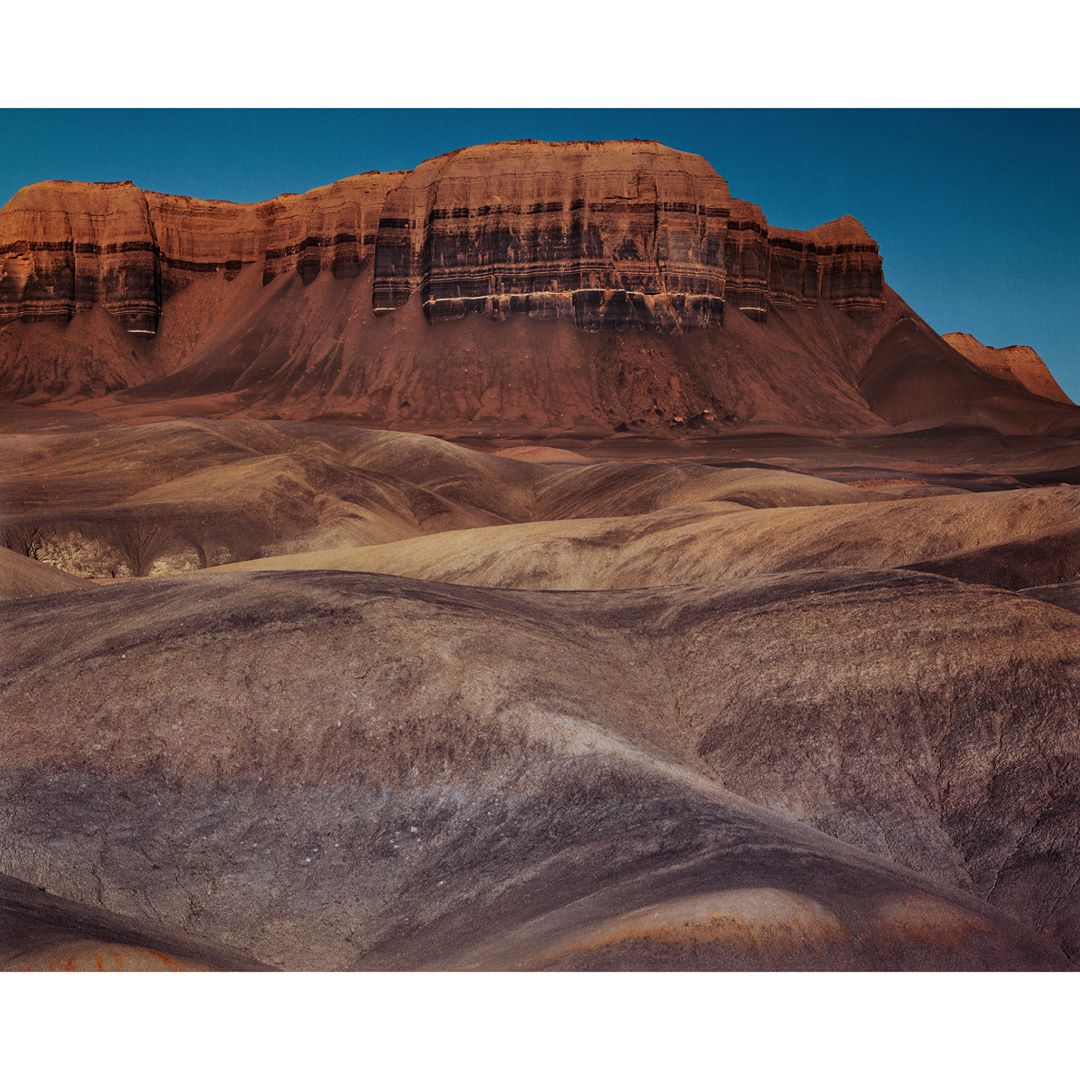 Panoramic landscape view of a large, flat-topped mesa, buttes, and desert terrain under a clear blue sky on a sunny day.