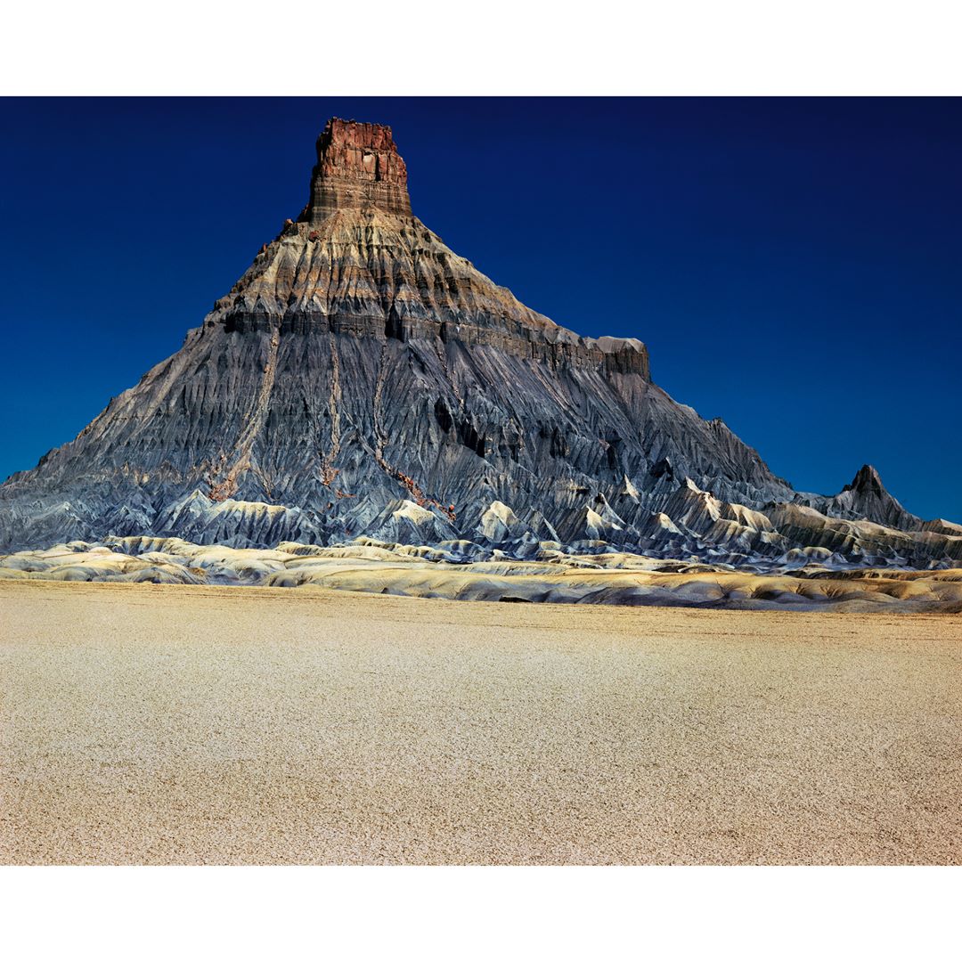 Daytime landscape of a large mesa formation in the Utah desert against a deep blue sky, highlighting the textures and rock formations.