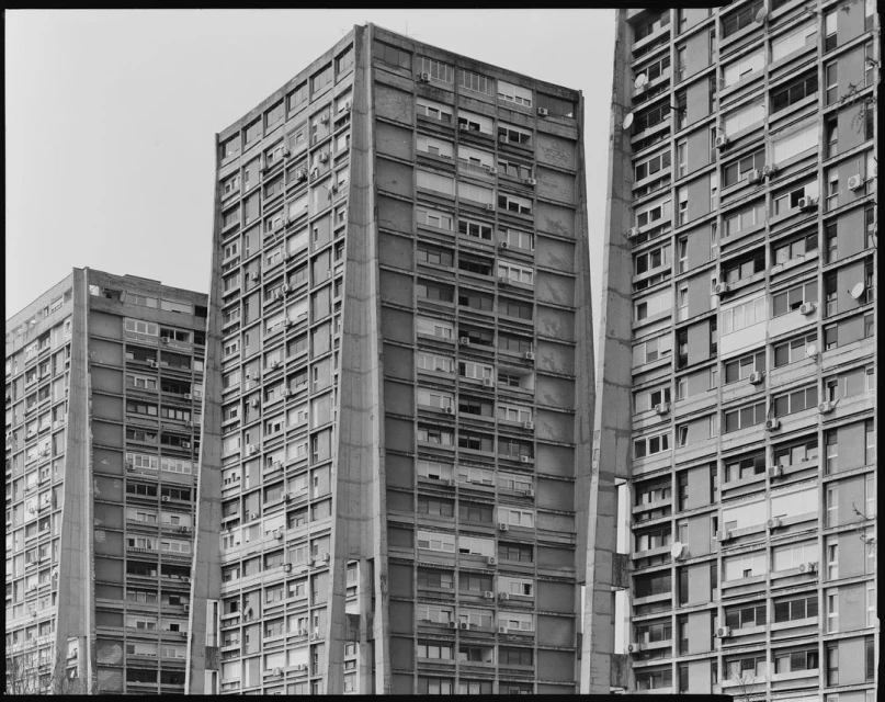 Low-angle black and white view of three concrete apartment buildings with multiple windows, creating a strong architectural statement.