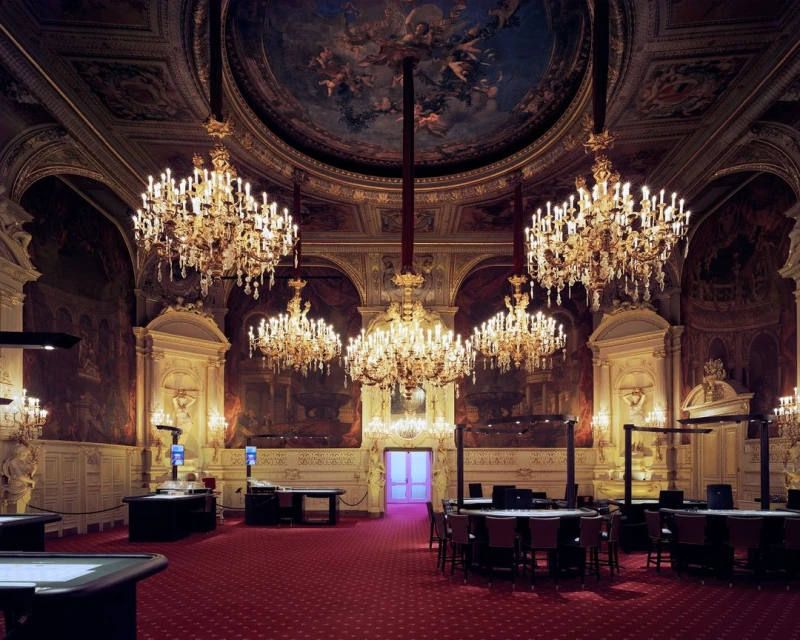 Ornate casino interior with crystal chandeliers, gaming tables, and detailed murals. Opulent architecture with a red carpet.